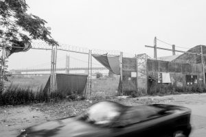 A car driving past a building on the street in a black and white outdoor setting.