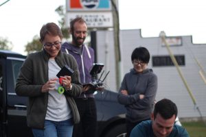 A group of people standing outside near a parked car under a clear sky.