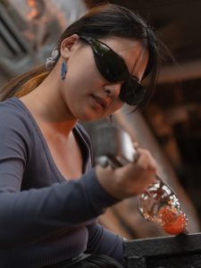 student blowing glass in glass hot shop