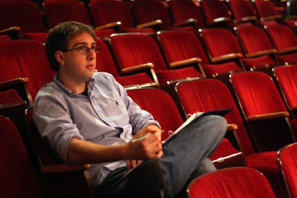 man sitting in red theatre seats and writing in book