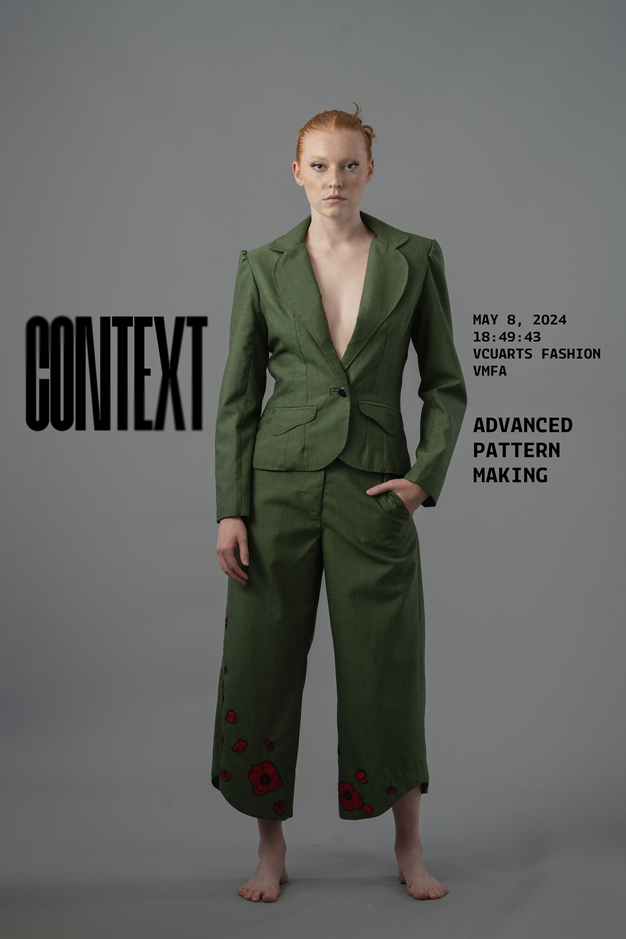 garment documentation of a model with red hair slicked back in a bun wearing a green suit jacket and pants with floral embroidery