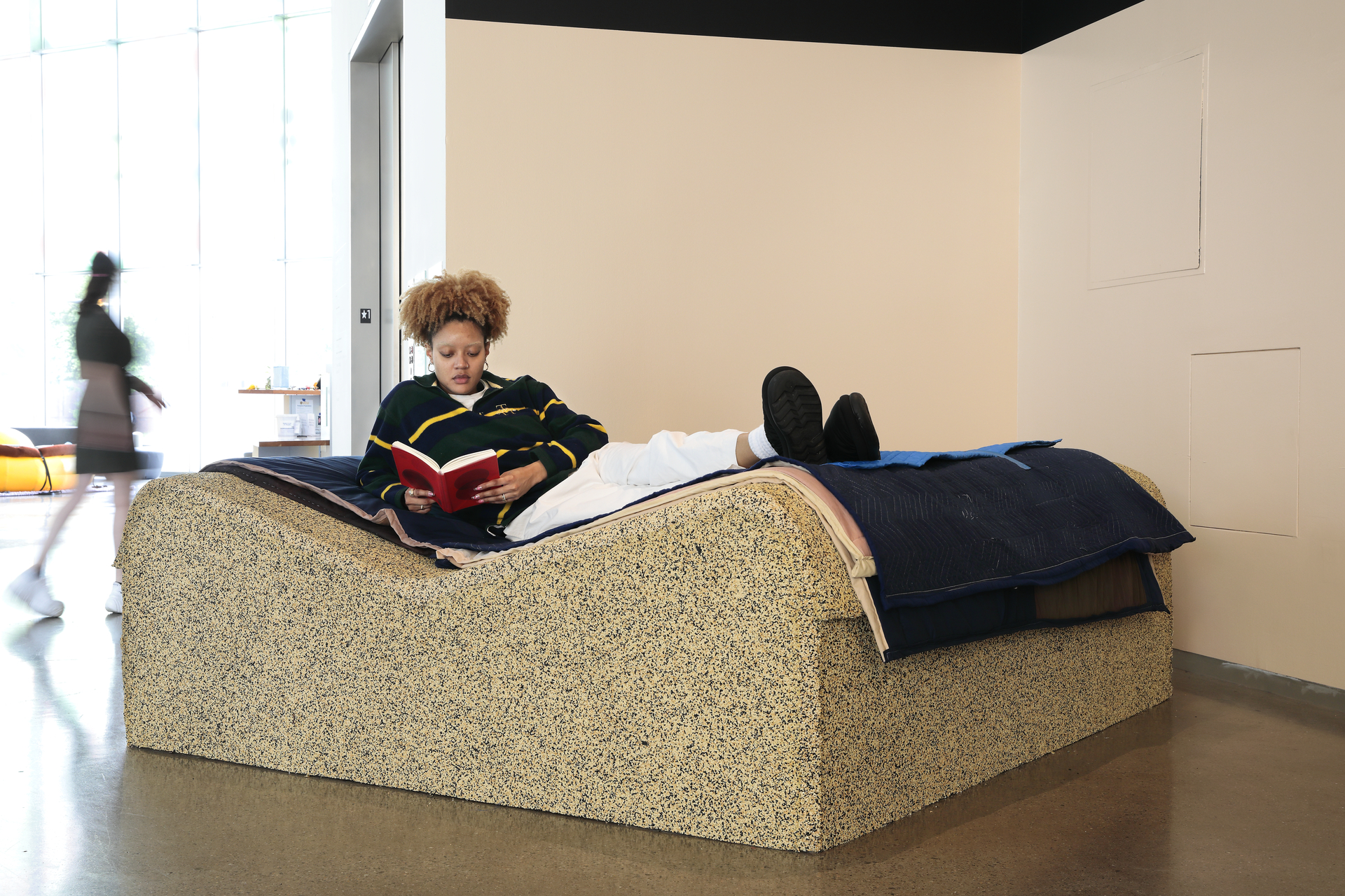 Student sitting in nicole killian's between a book and a soft place, 2023 installation and reading a book within the large scale, fabric pages of the seating sculpture