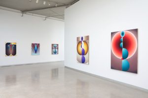 An exhibition view of Loie Hollowell's work showing two walls with 5 of Loie's brightly colored paintings of geometric and biomorphic forms.