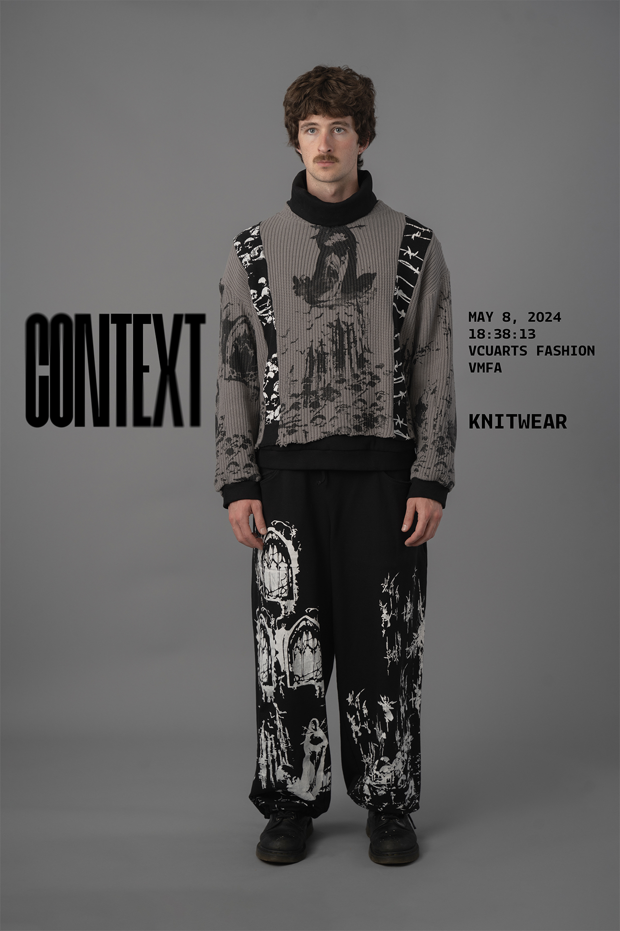 a model with cropped brown hair and a moustache wearing a grey knit sweater with black screenprinted punk inspired graphics and black sweatpants also screenprinted with white graphics