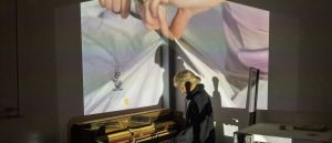 A student interacting with artwork combing a piano and projected imagery