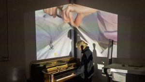 A student interacting with artwork combing a piano and projected imagery