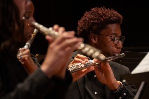 The Symphonic Wind Ensemble and University Band performing together and a student playing the flute