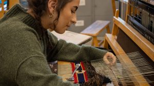 A student works at the loom on a tapestry project