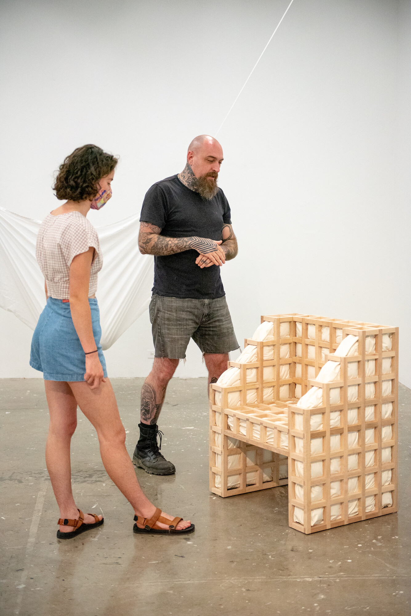 Secrets: squished is a functional chair with a wooden grid exoskeleton and protruding white cushions. The bulging cushions interrupt the architectural grid structure. Except for upholstery foam and batting, the contents of the cushions are known only to the artist.