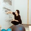 A student working on a graphite mural of a face on her studio wall