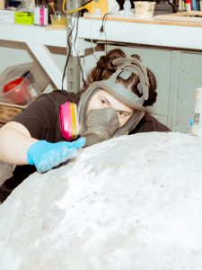 A student wearing protective breathing equipment builds a large round sculpture in their studio