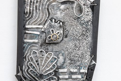 A silver aluminum sculpture etched with floral patterns in a black wooden frame