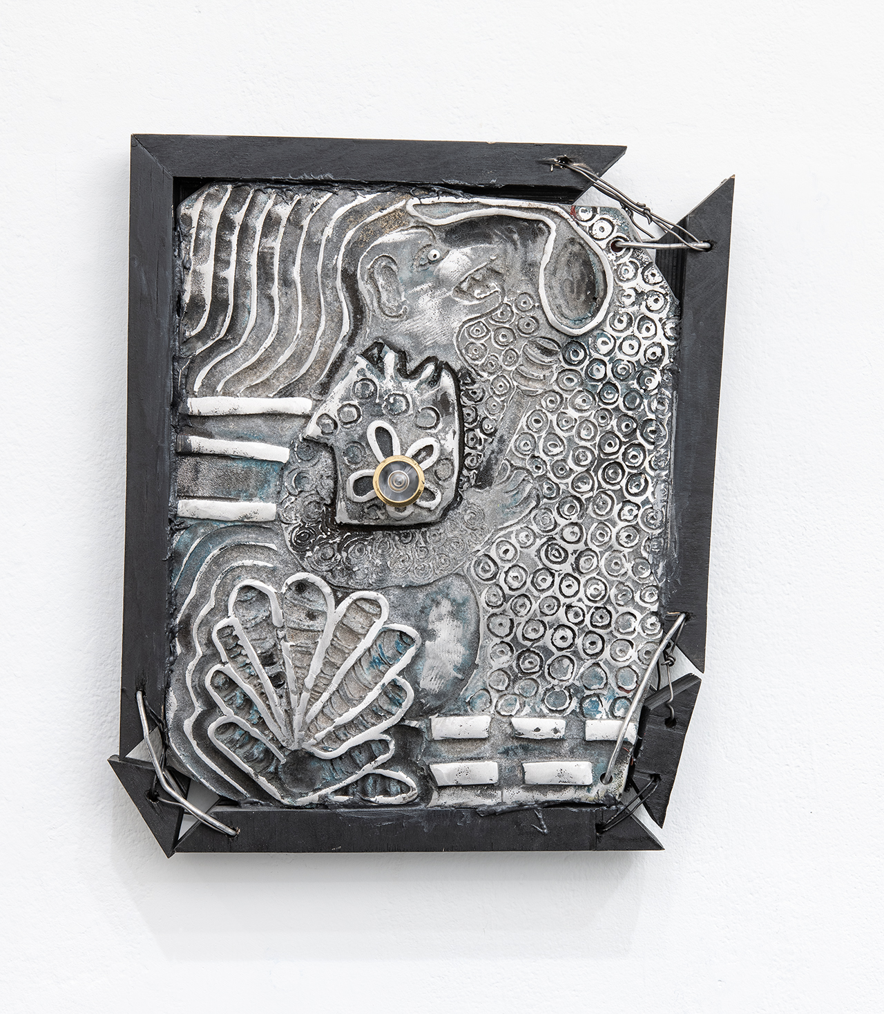 A silver aluminum sculpture etched with floral patterns in a black wooden frame