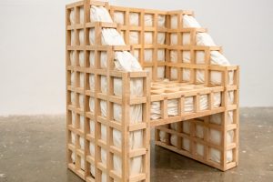 Secrets: squished is a functional chair with a wooden grid exoskeleton and protruding white cushions. The bulging cushions interrupt the architectural grid structure. Except for upholstery foam and batting, the contents of the cushions are known only to the artist.