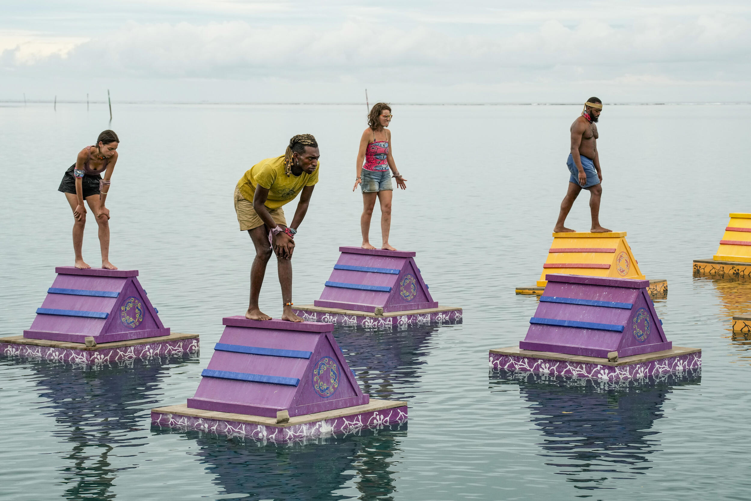 A photo of four people standing on triangular platforms that are on water. 