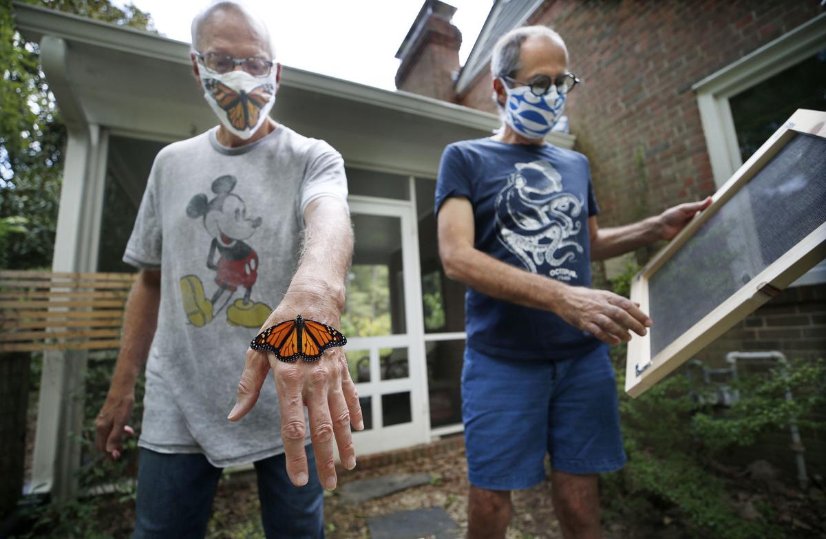 two men outside and one is holding a monarch butterfly