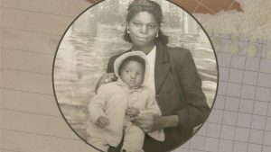 There is a pile of scrapbook paper with various colors and textures in the background. In the center, there is an old photo of a young black woman holding a baby on her lap. The baby is wearing a bonnet.