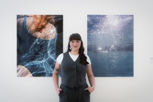 A woman standing in front of a wall adorned with various artworks in an art gallery setting.