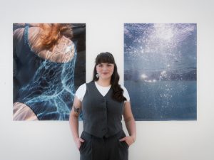 A woman standing in front of a wall adorned with various artworks in an art gallery setting.