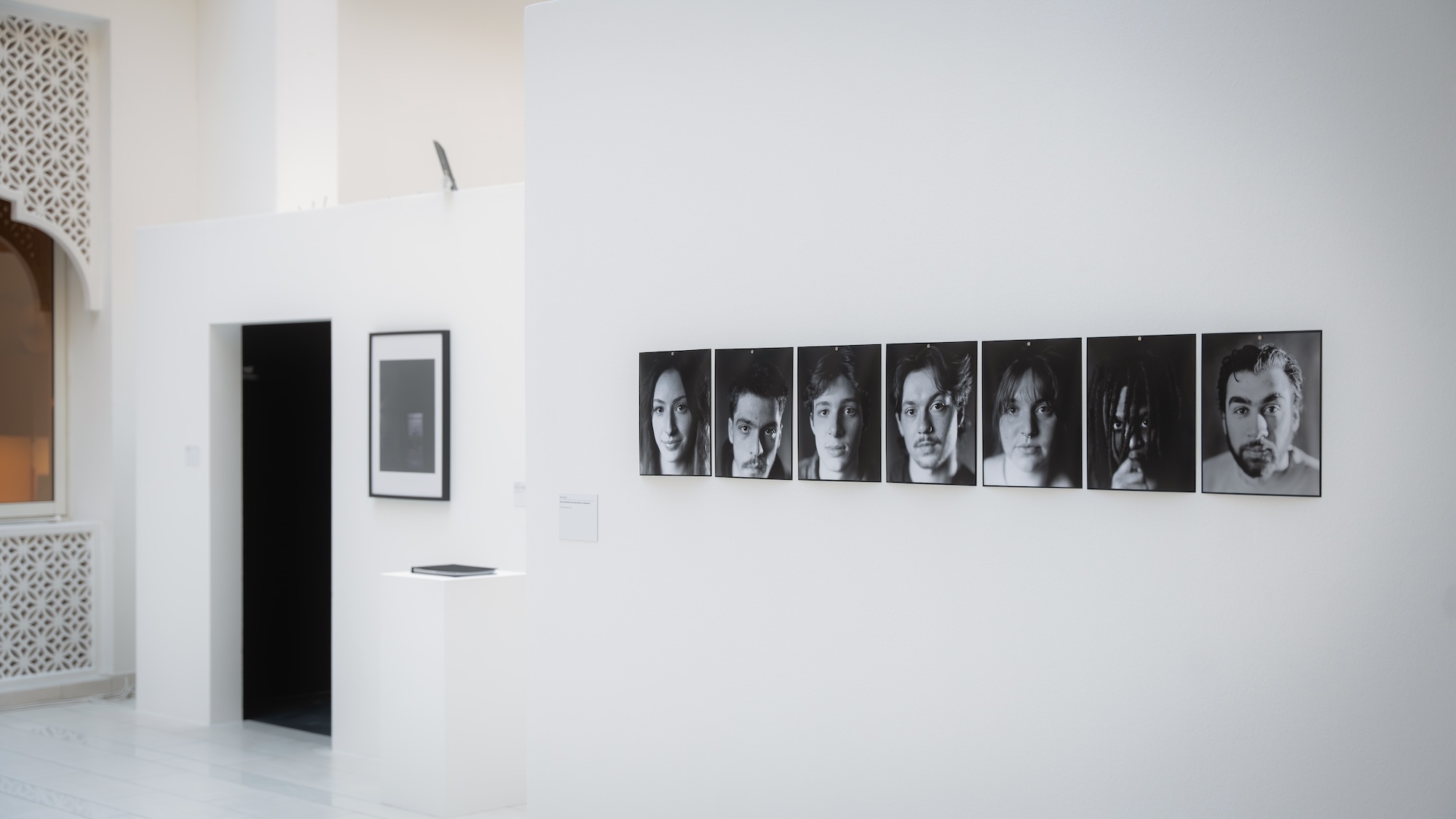 A wall in an indoor art gallery displaying various framed pictures, showcasing a range of portraits.