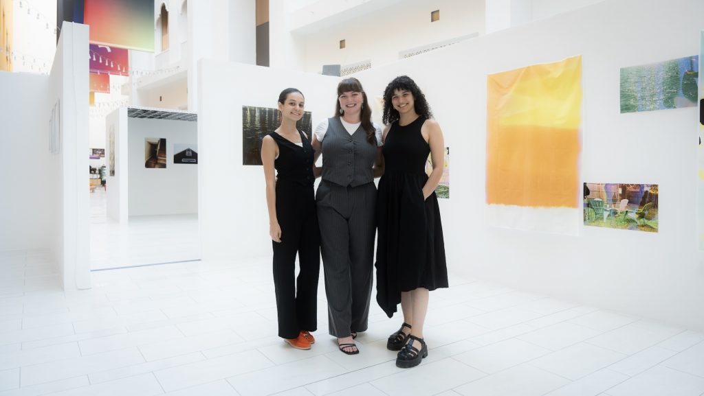 A group of people standing together for a photo in an art gallery, with various clothing styles and footwear, surrounded by artwork on the walls.