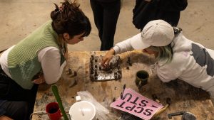 Two students are playing a ceramic chessboard. Next to them on the table is a sign reading "SCULPTURE."