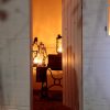 There is a white shed with its door open. Inside, there are three stretched gas lamps glowing in a dark room. There are on top of an old table and a box. On the exterior of the shed, above the doorframe, is "05/01" writing in charcoal.