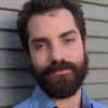 A bearded man looks at the camera.