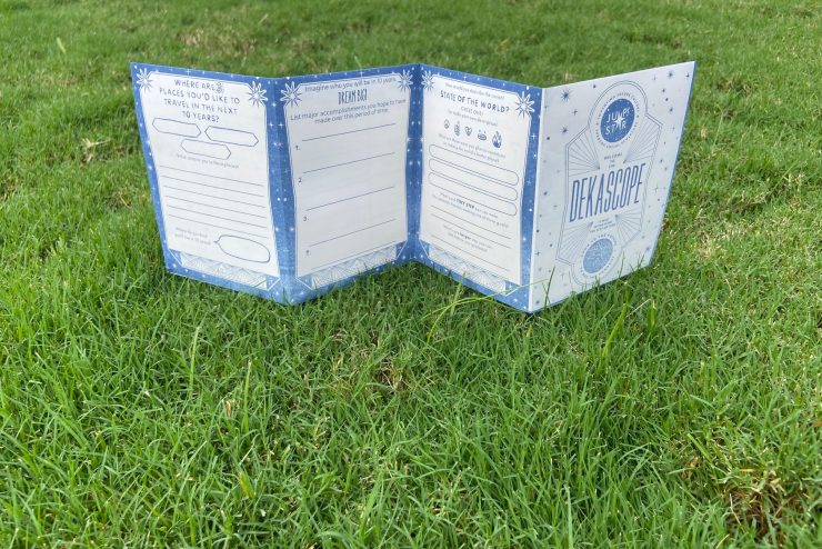 a folded zine with blue design elements sits on green grass