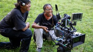 Two students from the Cinema program with alexa camera in a grassy field on location to film their summer students film.
