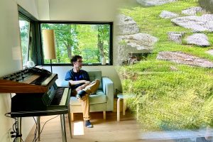 Stephen Vitiello sitting in a spring green living room, with electronic keyboard and soundboard equipment in view. Stephen looks to the viewer's right, where the reflection of a vibrant green hillside dotted with rocks captured in glass is superimposed over the right side of the room.