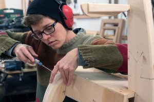 Katie is holding two pieces of wood. She is also holding a screwdriver as she joins the two pieces together.
