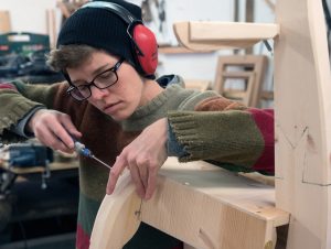 Katie is holding two pieces of wood. She is also holding a screwdriver as she joins the two pieces together.