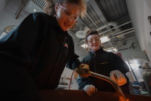 Student and faculty member are casting metal in the studio.